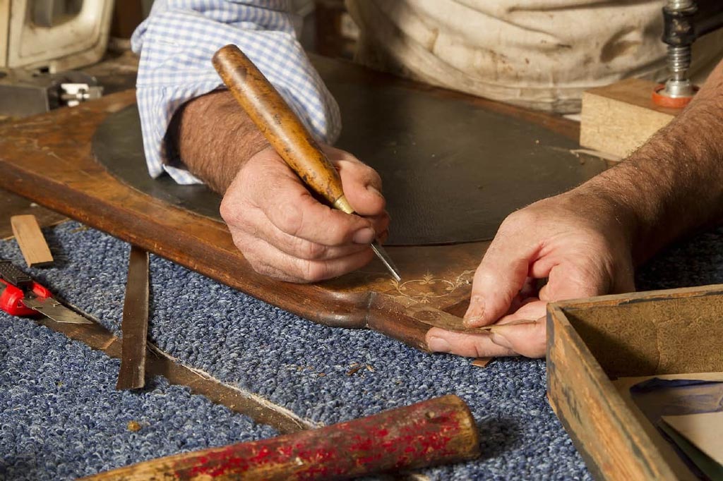 Proceso artesanal de un restaurador de muebles reparando madera.